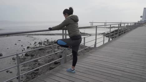 Concentrated-young-hindu-woman-warming-up-near-metal-railings-on-wooden-pier
